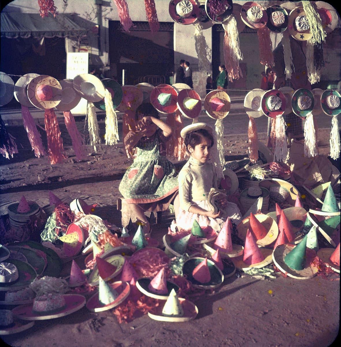 Niñas en un puesto de sombreros de cartón y papel, Recoleta, Región Metropolitana, Chile, 1950 - 1965
