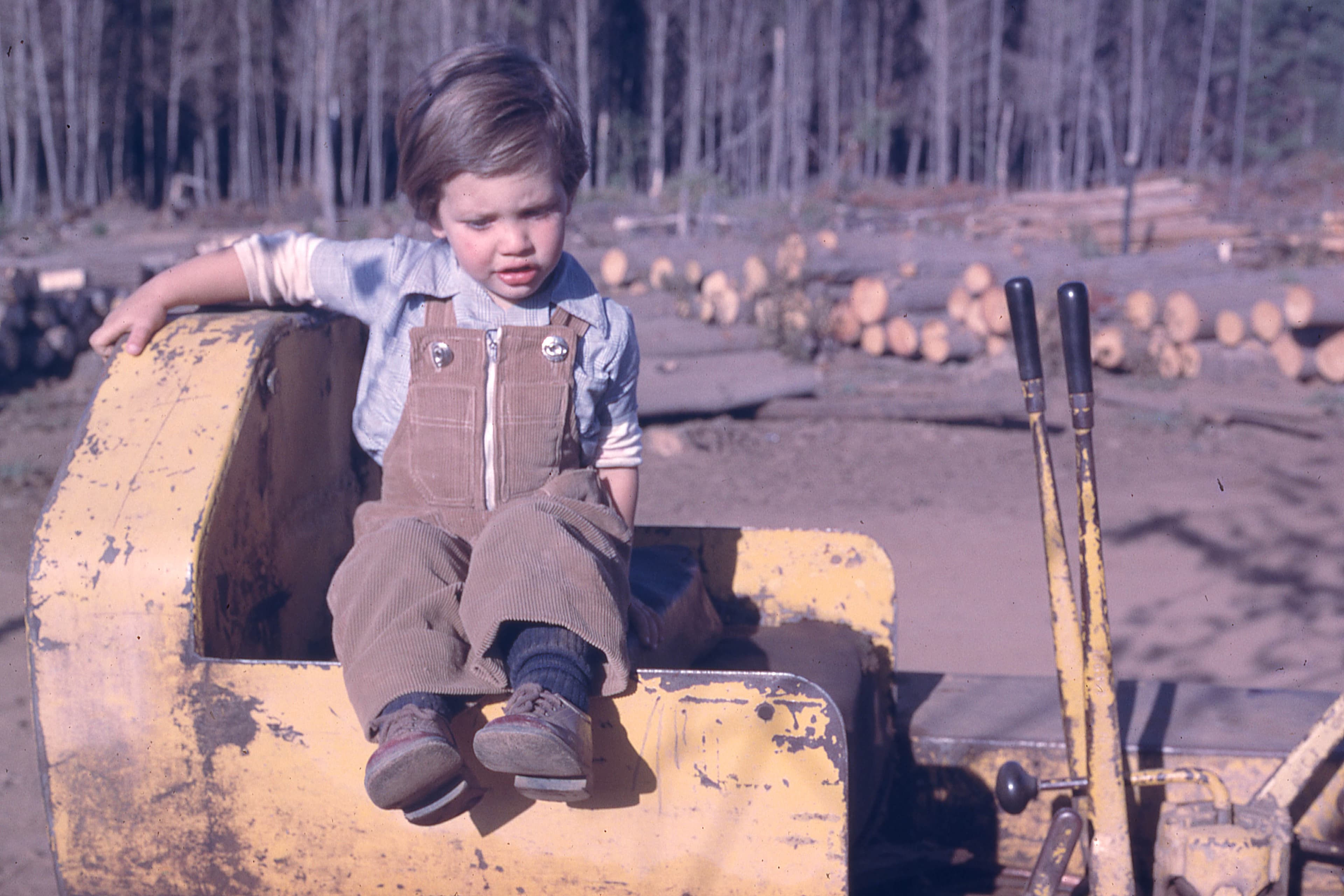 Niño sentado en maquinaria forestal, 1975